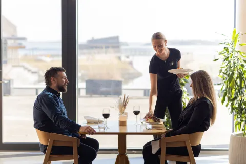 Servitør serverer to gjester mat i restauranten.
